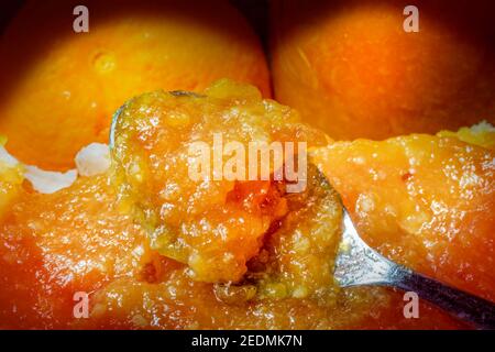 Löffel ertrank in frischer Orangenmarmelade. Über ein Stück Brot verteilen. Teil von Orange und Glas als Hintergrund Stockfoto