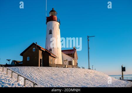 Winter in Urk mit dem Deich und Strand am Leuchtturm von Urk Schnee bedeckt im Winter, Sonnenuntergang am Leuchtturm von Urk Flevoland. Niederlande Stockfoto