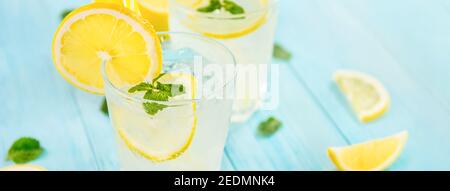 Erfrischende Getränke für den Sommer, kalter süß-saurer Limonensaft mit Eiswürfeln in den Gläsern garniert mit frisch geschnittenen Zitronen, Panorama-Banner Stockfoto