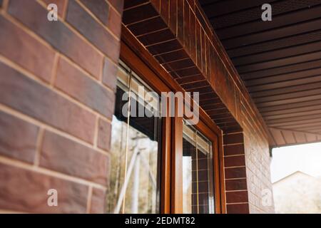 Fassadenverkleidung mit dunklen Keramikfliesen um das Fenster - Außenausführung im englischen Stil - rot glasierte Ziegelsteine Stockfoto
