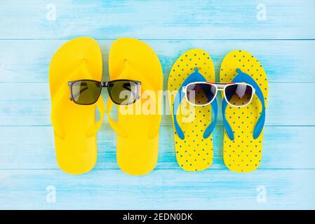 Bunte gelbe Flip-Flops mit Sonnenbrille für den Sommerurlaub am Strand, Draufsicht auf hellblauem Holz Hintergrund Stockfoto