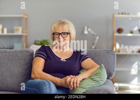 Positive ältere Frau Rentner Großmutter sitzt auf dem Sofa zu Hause Und Blick auf die Kamera Stockfoto