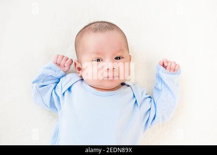 Neugeborenes hübsches Baby in der Schlafkleidung liegend auf weißem Laken, Ansicht von oben Stockfoto