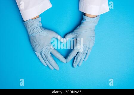 Zwei weibliche Hände in blauem Latex sterile medizinische Handschuhe zeigen eine Geste des Herzens auf blauem Hintergrund, Konzept der Güte, Hilfe und Freiwilligenarbeit Stockfoto