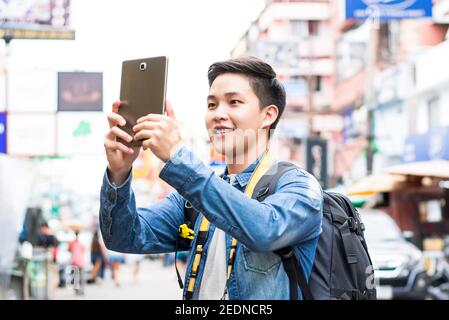 Junge asiatische Mann Tourist Backpacker Foto mit Tablet-Computer während der Reise auf Urlaub in Khaosan Road Bangkok, Thailand Stockfoto