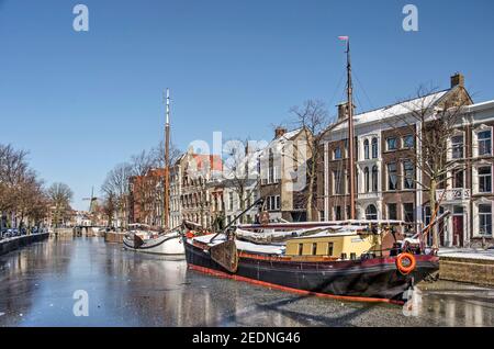 Schiedam, The Nethelrands, 11. Februar 2021: Historische Lastkähne im gefrorenen Long Harbour (lange Haven) Kanal an einem kalten, aber sonnigen Wintertag Stockfoto