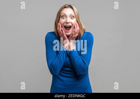 Unglaubliche Neuigkeiten! Portrait von glücklich überrascht Frau mit weit geöffnetem Mund und großen Augen halten die Hände auf das Gesicht, die durch plötzliche grosse Nachrichten schockiert. ind Stockfoto