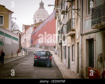 Lissabon, Portugal - 9. Feb 2018: Kartenfahrt auf einer winzigen Straße zwischen Gebäuden mit der Kirche Santa Engracia, auch bekannt als Nationales Pantheon, in der wichtige portugiesische Persönlichkeiten begraben sind Stockfoto