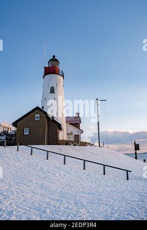 Winter in Urk mit dem Deich und Strand am Leuchtturm von Urk Schnee bedeckt im Winter, Sonnenuntergang am Leuchtturm von Urk Flevoland. Niederlande Stockfoto