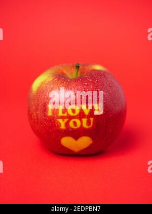 Valentinstag themed Apfel mit I Love You Nachricht und Ein Herzsymbol, das mit Wassertropfen bedeckt ist und auf das Symbol gesetzt wird Ein roter Hintergrund Stockfoto