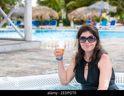 Porträt einer lächelnden Frau, die am Pool ein Bierglas hält Im Resort Stockfoto