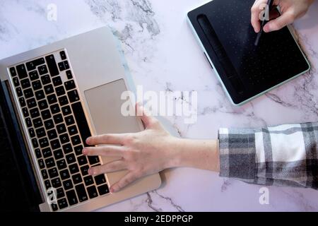 Draufsicht nicht erkennbare Geschäftsfrau tippt auf ihrem Laptop mit ihrem grafischen Tablet auf einem Marmorschreibtisch Hintergrund. Technologiekonzept. Kleinunternehmen Stockfoto