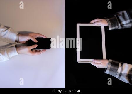 Nicht erkennbare Hände von Frau und Mann halten ein Tablet und Handy, die Yin Yang mit technologischer Ausrüstung. Technologiekonzept 2021. Stockfoto