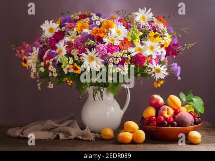 Blumenstrauß im Glas und frische Früchte Auf Holztisch Stockfoto