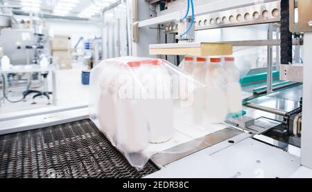 Milchfabrik Industrie, automatische Verpackung von Flaschen mit Milch in Plastiktüten. Stockfoto