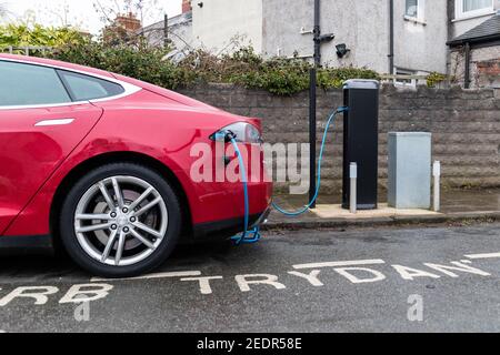 Cardiff, Wales, UK - Februar 14th 2021: Ein rotes Tesla-Elektroauto (EV) nutzt eine Ladestation, die von Cardiff Council bereitgestellt wird, in einer Wohnstraße. Stockfoto