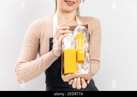 Meisterin Handwerker in Schürze hält verpackte fertige Produkt gelbe Kerzen aus Bienen Wachs mit Duft von Honig. Stockfoto