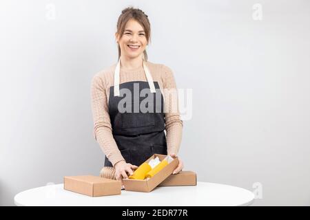 Meisterin Handwerker in Schürze hält verpackte fertige Produkt gelbe Kerzen aus Bienen Wachs mit Duft von Honig. Stockfoto