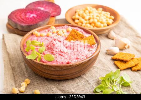 Hummus mit Rüben und mikrogrünen Basilikum Sprossen in Holzschüssel auf weißem Holzhintergrund und Leinentextilien. Seitenansicht, Nahaufnahme. Stockfoto