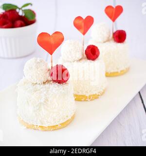 Dessert mit Kokosnussgeschmack und Himbeeren zum Valentinstag. Mini Käsekuchen in Einzelportionen. Stockfoto