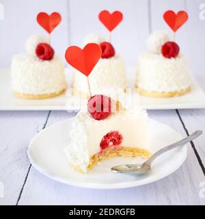 Dessert mit Kokosnussgeschmack und Himbeeren zum Valentinstag. Mini Käsekuchen in Einzelportionen. Stockfoto