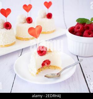 Dessert mit Kokosnussgeschmack und Himbeeren zum Valentinstag. Mini Käsekuchen in Einzelportionen. Stockfoto