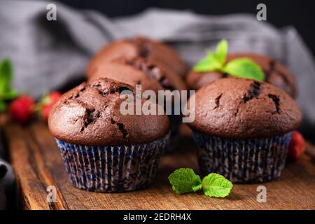 Schokoladenmuffins in violetten Pappbechern auf Holzbrett, Nahaufnahme. Leckere Schokoladen-Cupcakes ohne Sahne Stockfoto