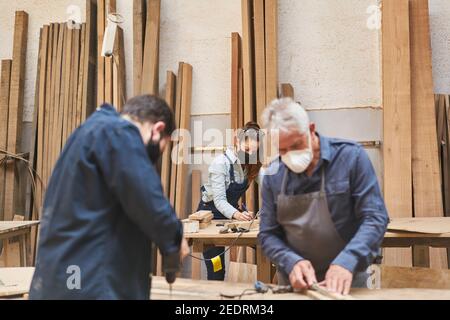 Handwerker Team mit Gesichtsmasken wegen Covid-19 arbeitet in Schreinerei Stockfoto