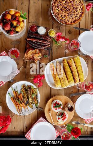 Esstisch mit Fleischgrill, Würstchen, Mais, gebratenes Gemüse, Saucen, Snacks und Limonade, Blick von oben, Familienessen oder Mittagessen, Esskonzept Stockfoto