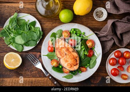 Gegrilltes Lachssteak mit Babyspinat und Kirschtomatensalat, Holztisch im Hintergrund, Draufsicht Stockfoto