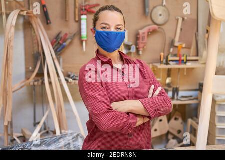 Junge Frau als Handwerker Auszubildende mit Gesichtsmaske weil Von Covid-19 in der Werkstatt Stockfoto