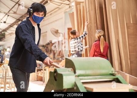 Junger Mann arbeitet als Handwerker mit Gesichtsmaske weil Von Covid-19 auf dem Hobel Stockfoto