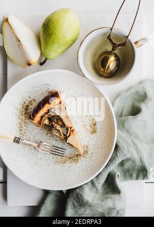 Flachlegen von vegan milchfrei zuckerfreien Birnen Käsekuchen Stück in rustikalem Teller, frische Birnen und Tasse für Tee auf weißem Marmortisch Hintergrund, Draufsicht. Modernes vegetarisches gesundes Dessertkonzept Stockfoto