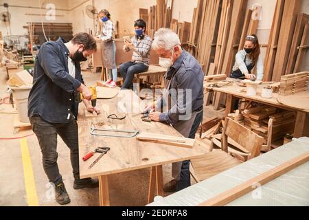 Gruppe von Handwerkern mit Gesichtsmasken wegen Covid-19 AT Arbeit in der Werkstatt Stockfoto