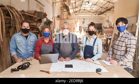 Gruppe von Handwerkern mit Gesichtsmasken wegen Covid-19 in Die Schreinerei Stockfoto