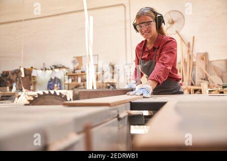 Junge Frau als Zimmermann in der Ausbildung arbeitet auf der Kreissäge der Schreinerei Stockfoto