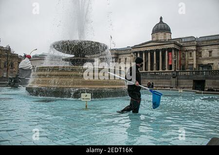 TRAFALGAR SQUARE LONDON, GROSSBRITANNIEN 15. FEBRUAR 2021. Ein Reinigungskraft des Westminster council holt Trümmer von den Brunnen am Trafalgar Square ab, während das Eis mit der wärmeren Wettervorhersage in den kommenden Tagen zu schmelzen beginnt. Eiszapfen hatten sich auf den eingefrorenen Brunnenskulpturen gebildet. Credit amer ghazzal/Alamy Live News Stockfoto