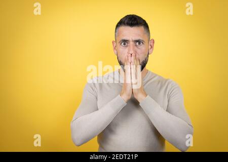 Schöner Mann mit Bart tragen Pullover über gelben Hintergrund schockiert Abdeckung Mund mit Händen für Fehler. Secret Konzept. Stockfoto