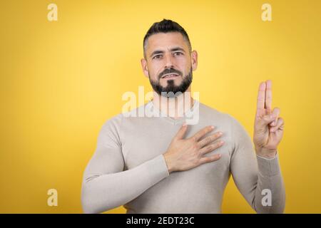 Hübscher Mann mit Bart trägt Pullover über gelben Hintergrund lächelnd Fluchen mit Hand auf Brust und Finger nach oben, so dass eine Treue Versprechen Eid Stockfoto