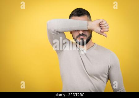 Schöner Mann mit Bart tragen Pullover über gelben Hintergrund Augen mit Arm lächelnd fröhlich und lustig. Blindes Konzept. Stockfoto