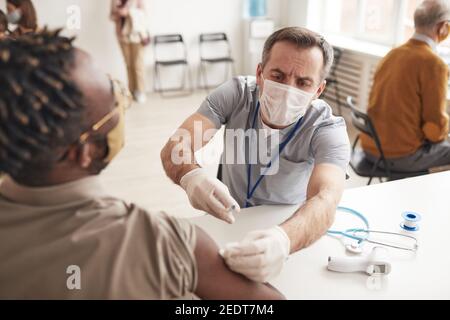 Porträt eines reifen männlichen Arztes, der afroamerikanischen Mann in einer medizinischen Klinik impft, Kopierraum Stockfoto