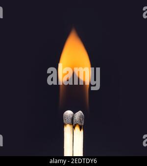 Herzförmige Flamme aus einem Paar brennender Streichhölzer auf schwarzem Hintergrund. Stockfoto