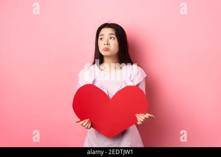 Valentinstagskonzept. Einsames Teenager asiatische Mädchen träumen von Liebe, traurig und einsam am Liebhabertag fühlen, mit Mitleid beiseite schauen, mit großen roten halten Stockfoto