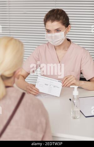 Vertikales Porträt einer jungen Krankenschwester, die während der Registrierung eine Maske trägt Patienten für covid Impfung im medizinischen Zentrum Stockfoto