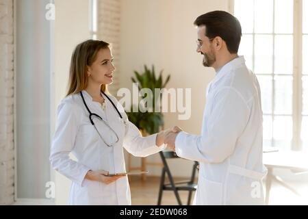 Lächelnd junge schöne Ärztin schüttelt sich die Hände mit Kollegen. Stockfoto
