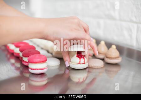 Nahaufnahme beschnittenes Bild von weiblichen Händen, die Verbindung der beiden Hälften Schalen von Makronen, mit Marmelade und Ganache verziert Stockfoto