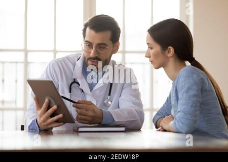 Fokussierter junger männlicher Arzt zeigt Ergebnisse auf Tablette für den Patienten. Stockfoto