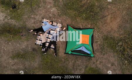 Luftaufnahme der Familie auf dem Campingplatz von oben, Eltern und Kind entspannen und liegen auf karierten, Familiencampingkonzept Stockfoto