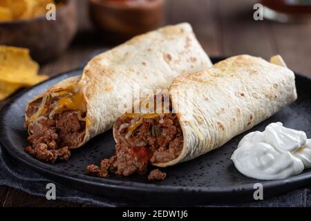 Nahaufnahme von zwei Rinderburritos und saurer Sahne auf einem Schwarze Platte Stockfoto