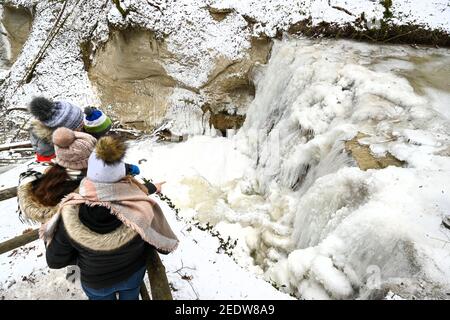 Ravensburg, Deutschland. Februar 2021, 15th. Faustdicke Eiszapfen hängen am Wasserfall im Rinkenburger Tobel, während eine Familie den Wasserfall von einer Aussichtsplattform aus betrachtet. Durch die Kälte ist der Wasserfall fast gefroren. Die Schlucht und der Wasserfall sind seit 2005 Natura 2000 Schutzgebiete der Europäischen Union. Quelle: Felix Kästle/dpa/Alamy Live News Stockfoto